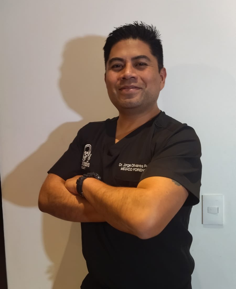 El Dr. Jorge Luis Olivares Peña, de brazos cruzados, con filipina negra de médico forense